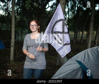 Una attivista femminile di Extinction Rebellion si trova fuori dalla sua tenda, tenendo una bandiera in un campeggio a Brockwell Park, Londra, 31 agosto 2020 Foto Stock