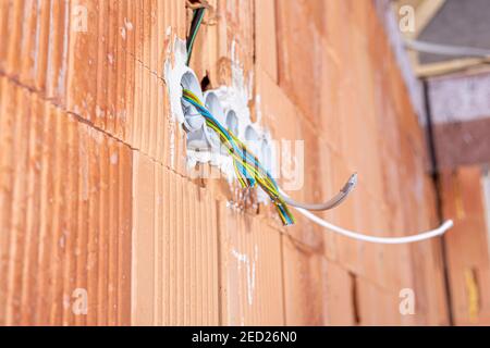 Scatole posteriori per prese con cavi in una parete. Sfondo del cablaggio. Fili elettrici colorati che fuoriescono dal foro delle prese elettriche sulla parete in mattoni. Nuovo ele Foto Stock