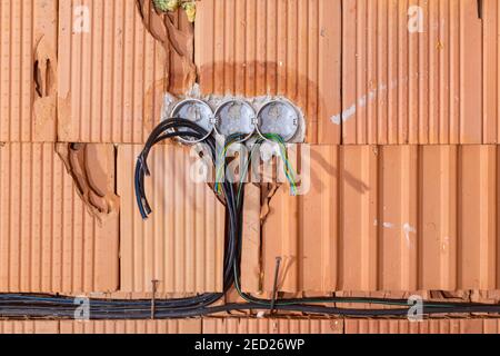 Scatole posteriori per prese con cavi in una parete. Sfondo del cablaggio. Fili elettrici colorati che fuoriescono dal foro delle prese elettriche sulla parete in mattoni. Nuovo ele Foto Stock