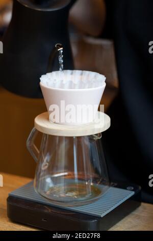 barista che versa l'acqua dal bollitore a kalita versare con filtro di carta su bilance digitali Foto Stock