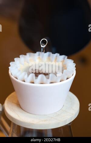 vista frontale del bollitore versando acqua calda in kalita versare sopra il filtro di carta e l'erogazione del caffè Foto Stock