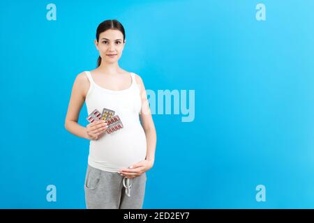 donna incinta che tiene supplementi materni su sfondo colorato con spazio di copia. Pillole in blister. Assistenza sanitaria durante il concetto di gravidanza. Foto Stock