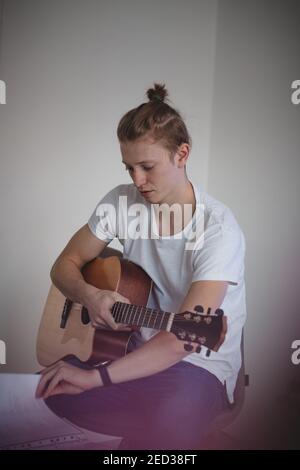 l'uomo con un fisico atletico si siede su uno sgabello e ribalta le pagine di un inno per selezionare la canzone appropriata. Sta tenendo una chitarra acustica. Afterno Foto Stock