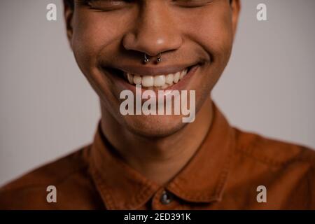 Primo piano foto di sorriso uomo nero e i suoi bei denti. Il maschio indossa una camicia, isolato sfondo grigio Foto Stock