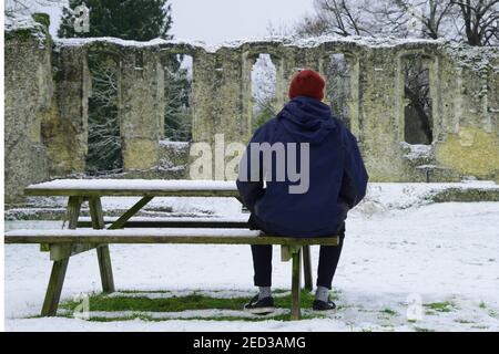 il giovane sedette sulla panchina nella neve guardando le rovine Foto Stock