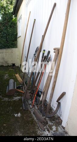 Vecchi attrezzi manuali da giardino appoggiati su una porta del garage. Foto Stock