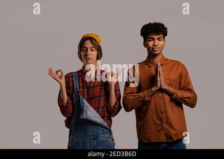 Foto di carino coppia contadini meditare e rilassarsi. Donna bianca indossa tuta in denim, camicia uomo nera isolato colore grigio sfondo Foto Stock