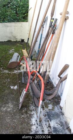 Vecchi attrezzi manuali da giardino appoggiati su una porta del garage. Foto Stock