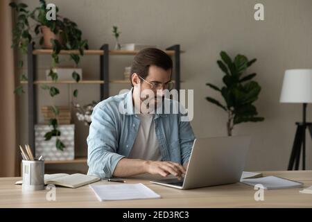 Freelance di giovani uomini d'affari focalizzato impegnato in un lavoro a distanza su un computer portatile Foto Stock