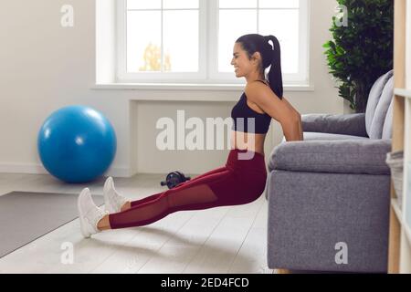 Donna in forma felice che fa i triceps tuffi o spinga-up inverso che afferrano bordo del divano a casa Foto Stock
