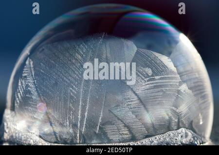 Macro di primo piano di una bolla di sapone congelata con schema astratto alla luce solare invernale, isolata in blu. Foto Stock