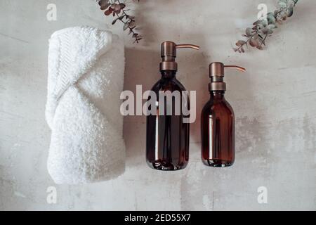 Dispenser per shampoo o flacone di sapone in vetro ambrato con pompa in acciaio al rame su fondo di pietra. Telo da bagno con eucalipto. Foto Stock