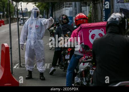 Un soldato filippino che indossa dispositivi di protezione individuale (PPE) controlla la temperatura corporea di un motociclista in un punto di controllo durante il blocco del coronavirus a Manila, Filippine. Foto Stock