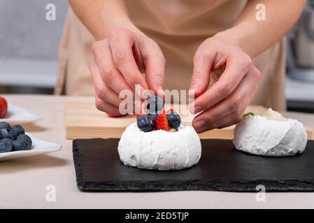 Mani femminili che decorano la meringa con mirtilli e fragole. Processo di fare torte. Foto Stock