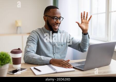 Uomo d'affari africano che fa la videochiamata in linea via laptop in ufficio Foto Stock