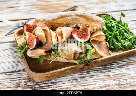 Sandwich con rucola, fico, prosciutto, ciabatta e formaggio blu su un vassoio di legno sfondo bianco. Vista dall'alto Foto Stock