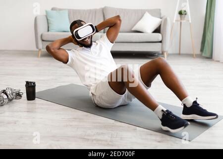 African Man indossare occhiali VR facendo esercizio ABS a casa Foto Stock