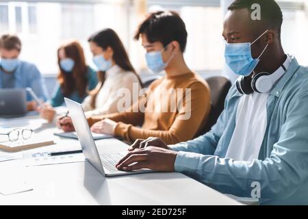 Studenti di persone internazionali che indossano maschere mediche utilizzando un computer portatile Foto Stock