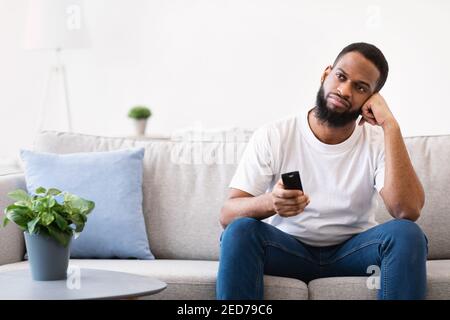 Annoiato uomo africano che guarda la TV che cambia canali televisivi a casa Foto Stock