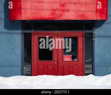 Ingresso a porte rosse con un cartello chiuso su un edificio blu bloccato da una banca di neve a Speculator, NY USA Foto Stock