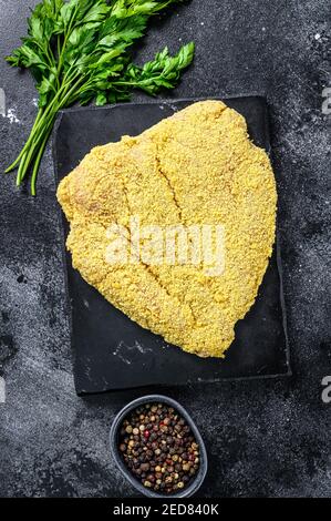 Greggia grande schnitzel viennese su un tagliere. Sfondo nero. Vista dall'alto Foto Stock