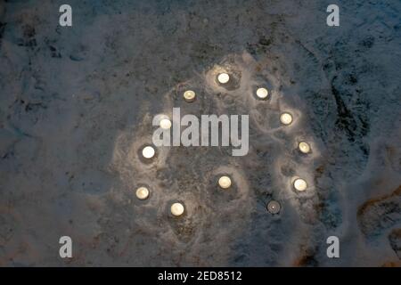Piccole candele circolari illuminate che fanno il contorno del cuore sul neve di notte Foto Stock