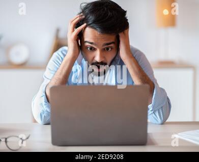 Stress di scadenza. Uomo arabo che guarda lo schermo del notebook, tocca la testa sotto shock Foto Stock