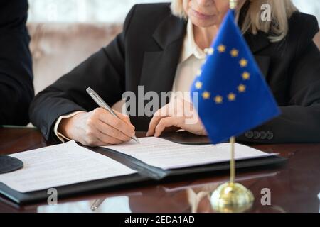 Bandiera dell'Unione europea sul tavolo contro la delegata femminile matura firma del contratto dopo la negoziazione e la conclusione di un accordo per tavolo sala riunioni Foto Stock