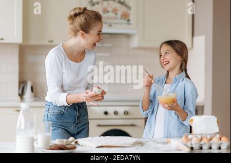 La mamma caucasica felice e la sua amata piccola figlia trascorrono il tempo insieme in cucina. Mamma insegna alla figlia a cucinare, sono felici di cucinare insieme Foto Stock