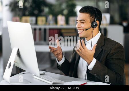 Leader, manager o tutor ispanici di successo, seduti alla scrivania indossando le cuffie, comunicano e sorridono durante una videoconferenza con colleghi o studenti Foto Stock