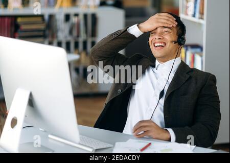 Sorridente business leader, manager o tutor ispanico di successo seduto al tavolo da lavoro con cuffie e sorridente durante una videoconferenza con colleghi o studenti Foto Stock