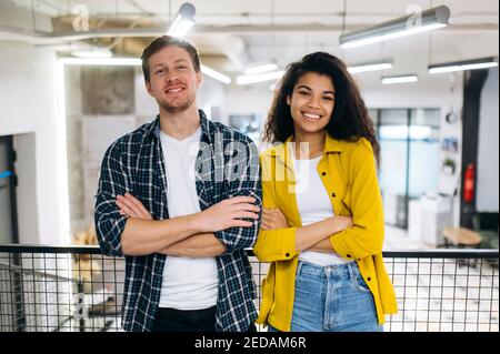 Ritratto di colleghi di lavoro o amici studenti. Bell'uomo caucasico e bella donna afroamericana lavorano o studiano insieme. I colleghi multirazziali dei giovani adulti guardano la telecamera sorridendo Foto Stock