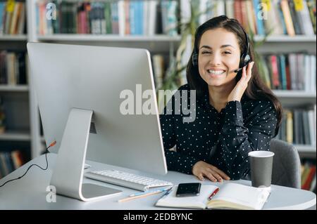 Ritratto della donna caucasica operatore del call center. Felice consulente femminile seduto al tavolo, indossando le cuffie, parlando con i clienti, servizio di supporto concetto Foto Stock