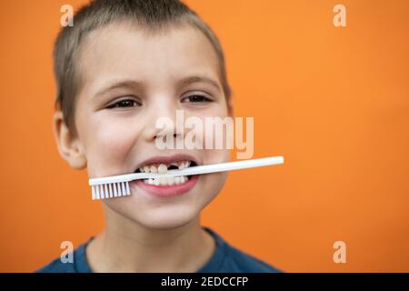 Il ragazzo senza il dente superiore del latte in una t-shirt blu tiene lo spazzolino in bocca su sfondo arancione. Foto Stock