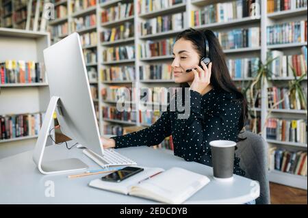 Elegante donna manager che utilizza un laptop e una cuffia, lavorando in un centro di assistenza. Bella operatore femminile di call center è la consulenza di un cliente, comunicare con persone diverse Foto Stock