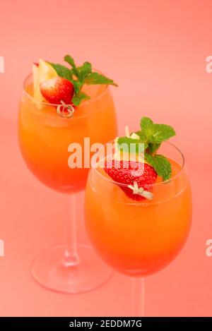 Cocktail colorati e rinfrescanti all'alba con fragola e arancio nei bicchieri su sfondo rosa corallo Foto Stock