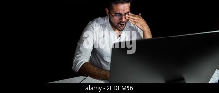 Stanco uomo d'affari asiatico stanco che si sente sonnolento e sbadigliato mentre lavora turno notturno davanti al computer Foto Stock