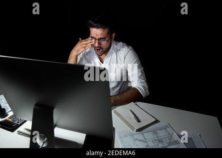 Stanco uomo d'affari asiatico stanco che si sente sonnolento e sbadigliato mentre lavora turno notturno davanti al computer Foto Stock