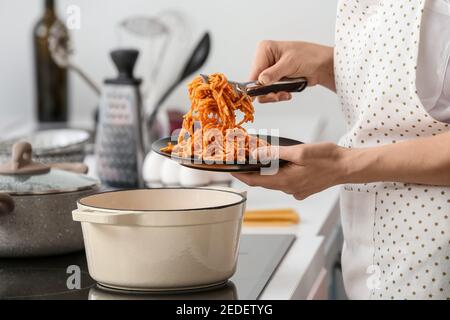 Donna che mette la pasta gustosa sul piatto dal piatto di cottura dentro cucina Foto Stock