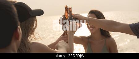 Gruppo di amici che hanno festeggiato festa claging bottiglie di birra fare un brindisi prima di bere alla spiaggia al crepuscolo, banner panoramico Foto Stock