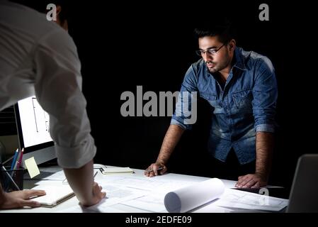 Architetto asiatico o team di ingegneri che soggiornano fino a tarda notte l'ufficio che discute il progetto al tavolo della riunione Foto Stock