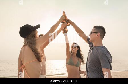 Gruppo di amici che argillano bottiglie di birra con festa festiva e. bere in spiaggia in estate Foto Stock