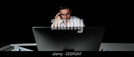 Serio uomo d'affari asiatico che lavora a tarda notte in ufficio guardando lo schermo del computer e pensando, banner panoramico Foto Stock