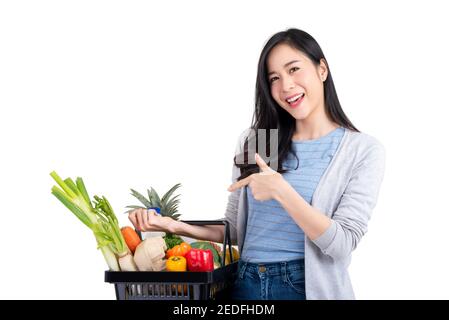 Bella donna asiatica che tiene il cestino della spesa pieno di verdure e generi alimentari, studio girato isolato su sfondo bianco Foto Stock