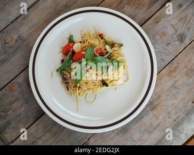 Spaghetti misti con pesce salato con peperoncino al basilico e pomodoro rosso, fusion food italiano in un piatto bianco su tavola di legno marrone Foto Stock