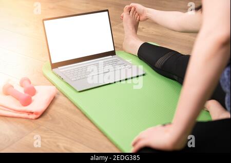 Formazione online a casa. Donna che si esercita a casa di fronte al suo laptop, allungando le gambe. Donna che fa l'allenamento yoga a casa guardando i video on-line Foto Stock