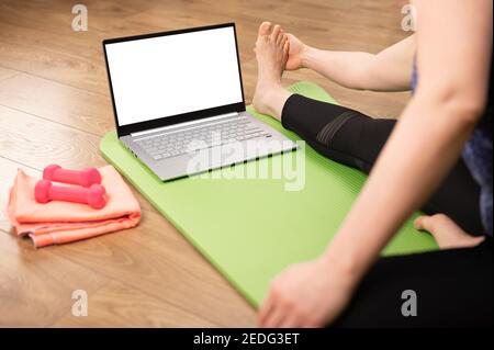 donna che fa yoga stretching yoga on-line a casa. guardare una lezione di yoga on-line sul computer portatile. Donna stretching online con laptop su tappetino yoga a hom Foto Stock