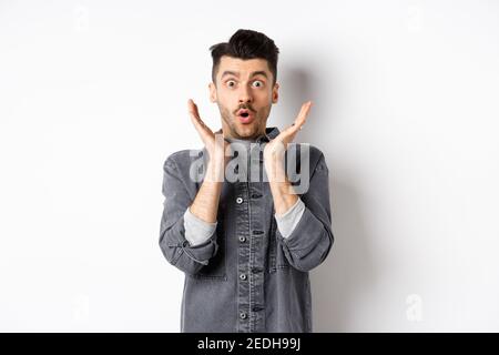 L'uomo sorpreso che gasting eccitato, dica WOW e guardi la pubblicità stupefacente, in piedi su sfondo bianco Foto Stock