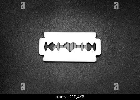 La lama del rasoio a superficie speculare con un'apertura a forma di cuore nella al centro su uno sfondo nero Foto Stock