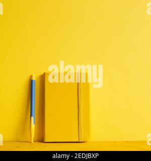 Taccuino giallo e penna su tavolo di legno. Sfondo giallo Foto Stock